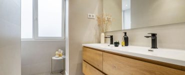 Une salle de bains avec double évier, robinets noirs et armoire en bois couleur châtaignier
