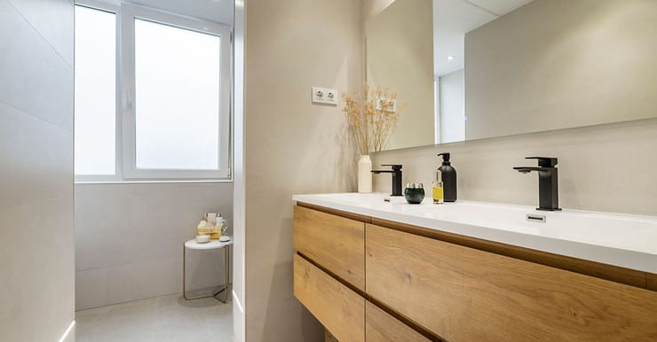 Une salle de bains avec double évier, robinets noirs et armoire en bois couleur châtaignier