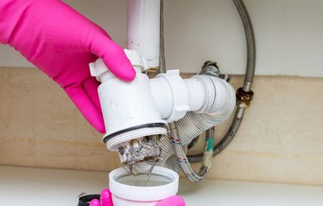 Des mains dans des gants en caoutchouc rose en train de vider le siphon plein de crasses