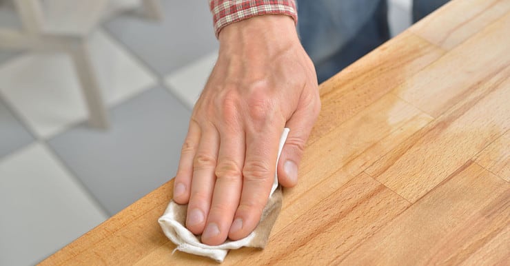 Zoom sur la main d'un homme appliquant un produit sur le comptoir d'une cuisine en bois de hêtre