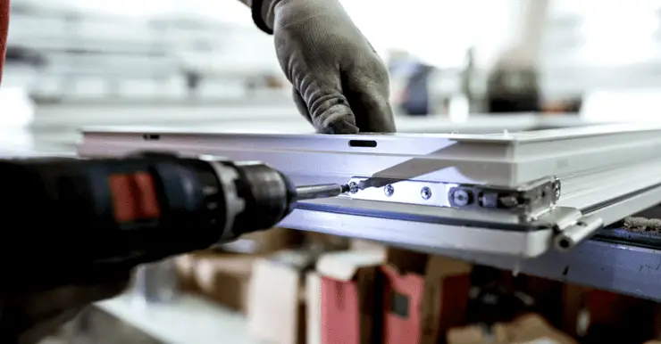 Un homme en train d'assembler une fenêtre en aluminium à l'aide de son perceuse visseuse