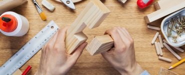 Un homme tient dans ses mains deux éléments en bois pour un assemblage en croix