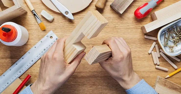 Un homme tient dans ses mains deux éléments en bois pour un assemblage en croix