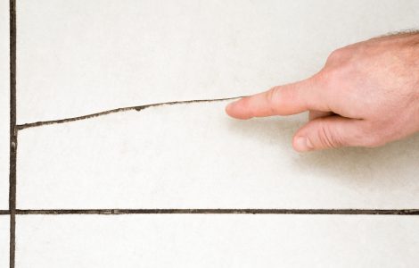 Une main montrant du doigt une fissure dans le carrelage