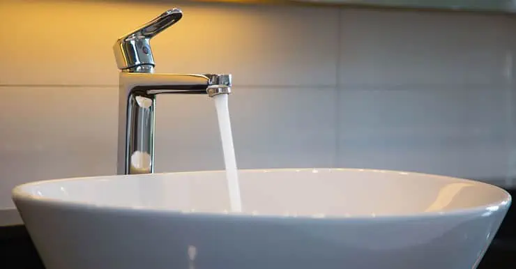 Une vasque de salle de bain avec un robinet ouvert laissant couler l’eau