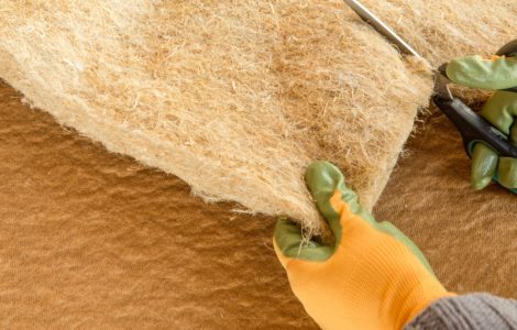 Zoom sur les mains d’une personne en gants verts et jaunes, découpant une couche d’isolation avec un ciseau