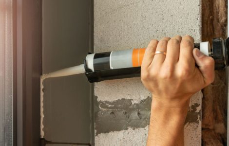 Zoom sur les mains d'un homme applicant un joint en silicone avec un pistolet à colle