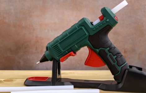Un pistolet à colle chaude et des bâtons de colle blanche posés sur une table en bois