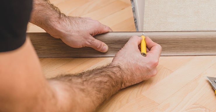 Un homme marque la plinthe au crayon avant la découpe et la pose