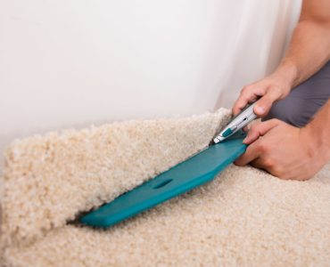 Un homme installant une moquette coupe ce qui dépasse avec un cutter