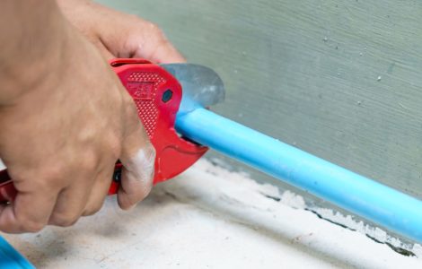 Zoom sur la main d’un homme utilisant un coupe-tube pour couper un tuyau bleu