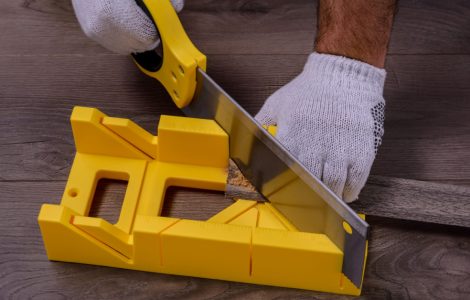 Zoom sur les mains d’un homme qui coupe une planche à l’aide d’une scie et d’une boîte à onglets