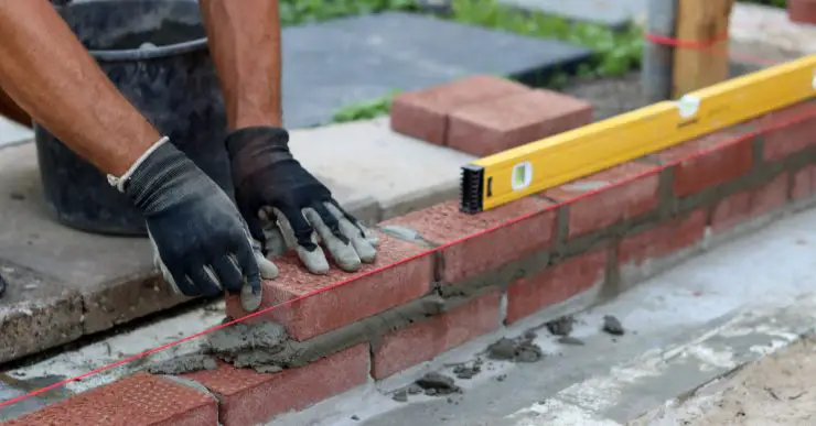 Un homme constuit un mur en briques tout en vérifiant le niveau