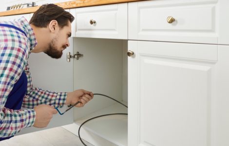 Un plombier en train de déboucher les canalisations d'un évier à l'aide d'un furet