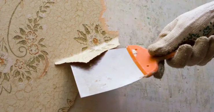 Main d'un homme en train de décoller du papier peint avec un outil