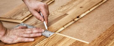 Zoom sur les mains d'un homme traçant la découpe d'un parquet en bois