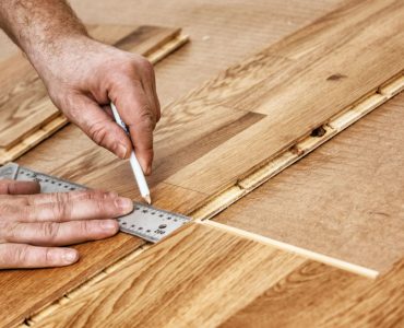 Zoom sur les mains d'un homme traçant la découpe d'un parquet en bois