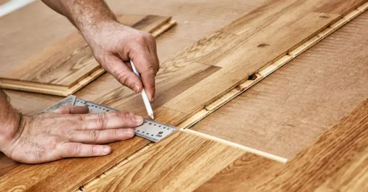 Zoom sur les mains d'un homme traçant la découpe d'un parquet en bois