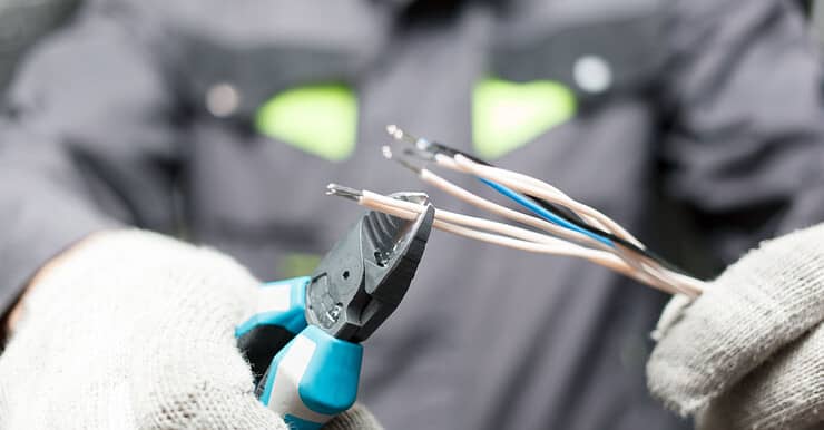 Une personne en gants blancs en train de dénuder des fils électriques avec une pince