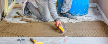 Un homme étale de la colle mortier pour la pose du carrelage de sol