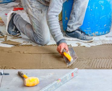 Un homme étale de la colle mortier pour la pose du carrelage de sol