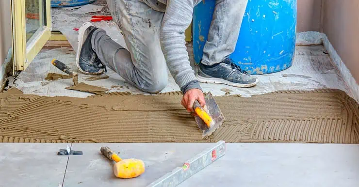 Un homme étale de la colle mortier pour la pose du carrelage de sol