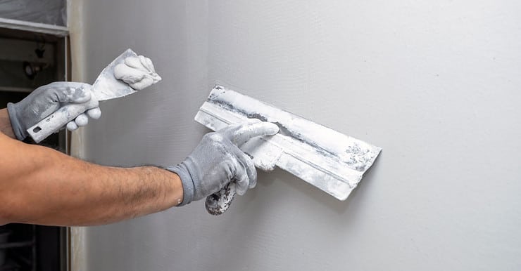 Zoom sur les mains d’un homme étalant un enduit sur le mur avec une spatule