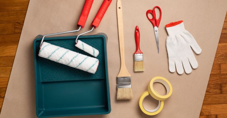 Différents outils pour la peinture posés sur la table : rouleau, pinceau, gant…