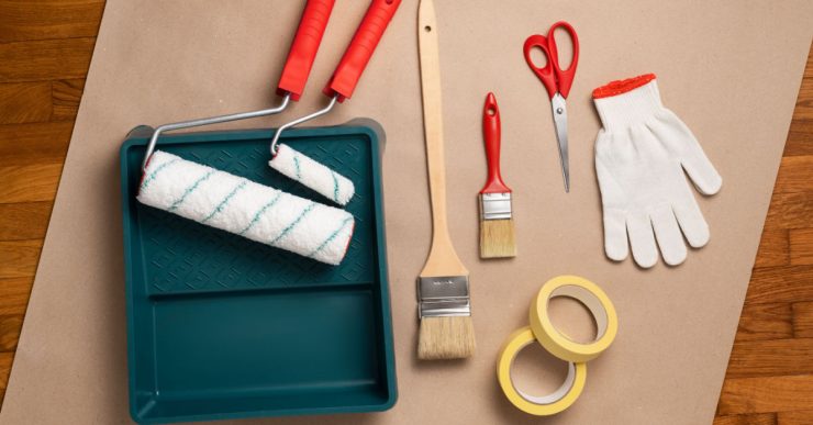 Différents outils pour la peinture posés sur la table : rouleau, pinceau, gant…