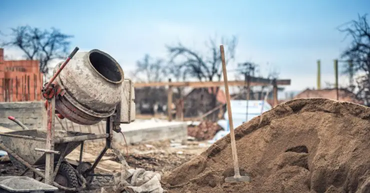 Une petite bétonnière, une brouette, une pelle et du sable dans un chantier