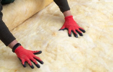 Un homme en gants rouges pose de la laine minérale sur le sol