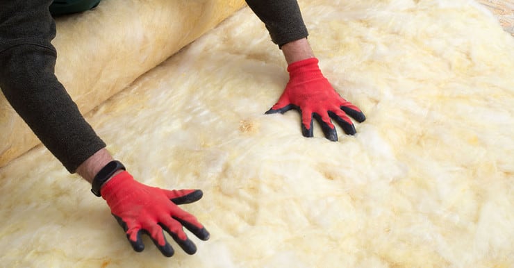 Un homme en gants rouges pose de la laine minérale sur le sol
