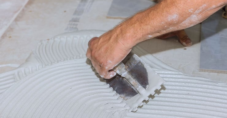 Zoom sur les mains d'un homme appliquant du mortier avant de poser le carrelage de sol