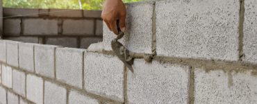 Un homme contruit un mur en parpaings avec sa truelle