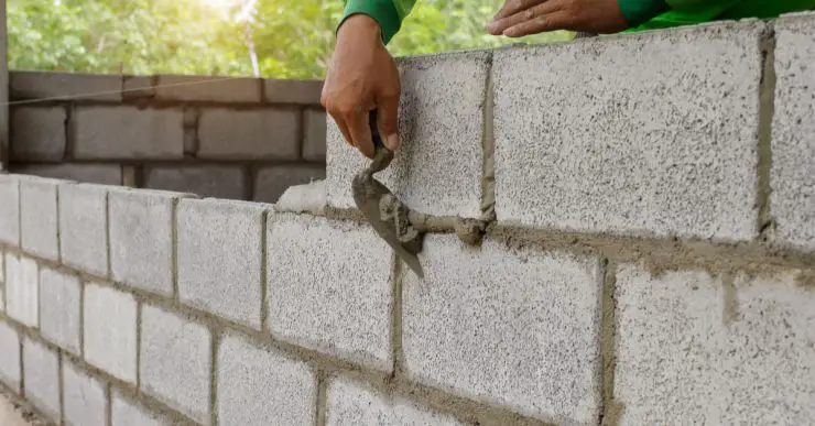 Un homme contruit un mur en parpaings avec sa truelle