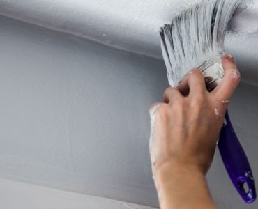 Zoom sur la main d’un homme peignant le plafond à l’aide d’un pinceau