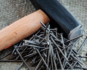 Un marteau avec manche en bois posé à côté de plusieurs clous