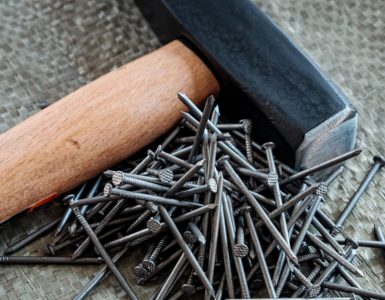 Un marteau avec manche en bois posé à côté de plusieurs clous