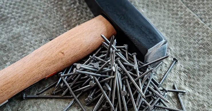 Un marteau avec manche en bois posé à côté de plusieurs clous