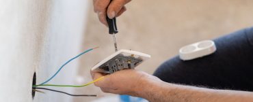 Zoom sur les mains d’un homme installant une prise électrique sur le mur