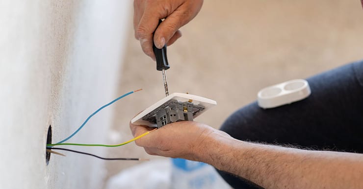 Zoom sur les mains d’un homme installant une prise électrique sur le mur