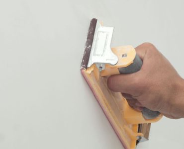 Zoom sur la main d’un homme grattant un mur avec du papier de verre