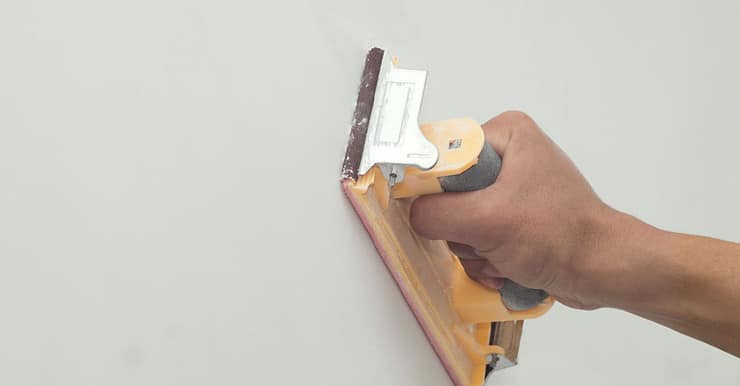 Zoom sur la main d’un homme grattant un mur avec du papier de verre