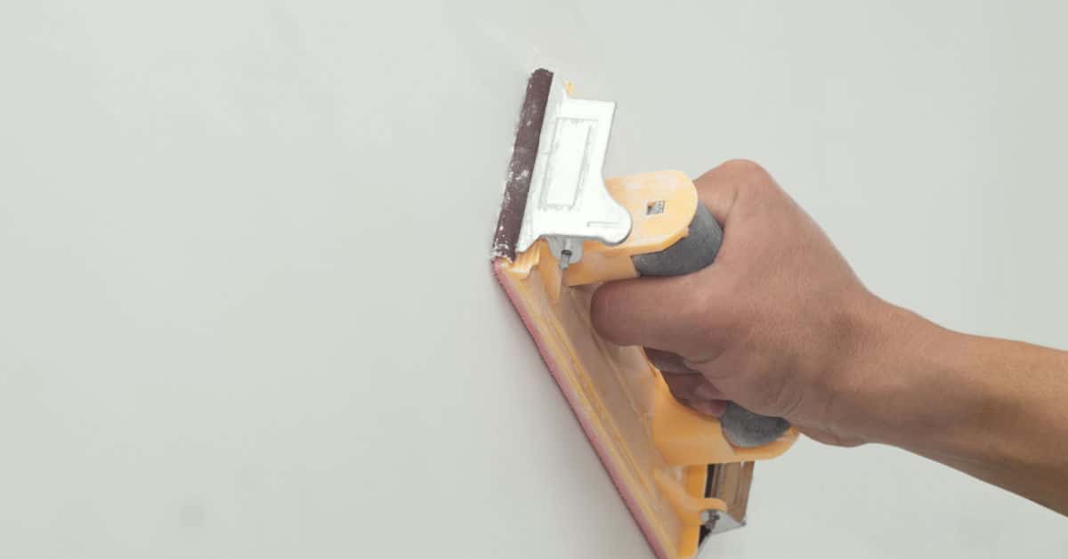 Zoom sur la main d’un homme grattant un mur avec du papier de verre