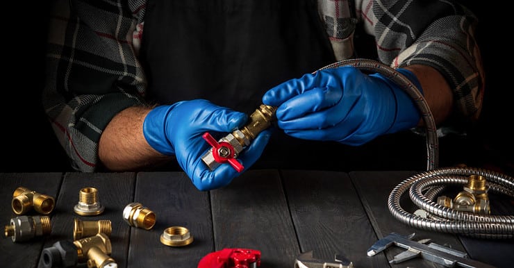 Un homme en gants bleus connecte les raccords en laiton d’un équipement de gaz