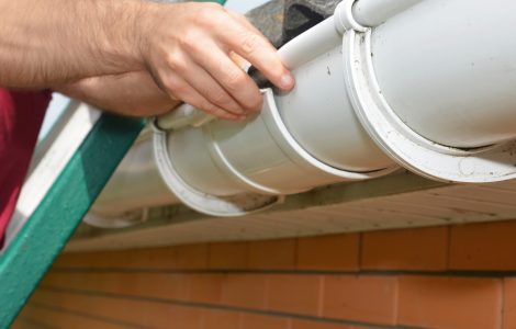 Un homme est monté sur l'escalier pour réparer une gouttière blanche