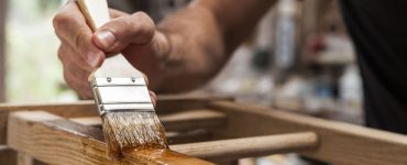 Zoom sur la main d’un homme tenant une brosse et appliquant du vernis sur un mobilier en bois