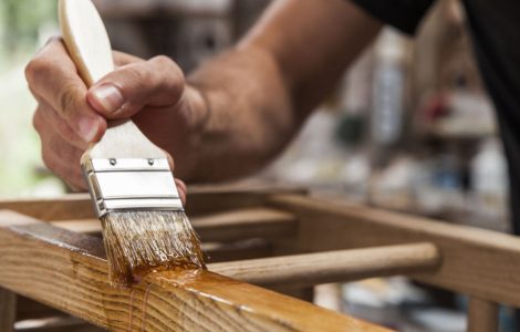 Zoom sur la main d’un homme tenant une brosse et appliquant du vernis sur un mobilier en bois