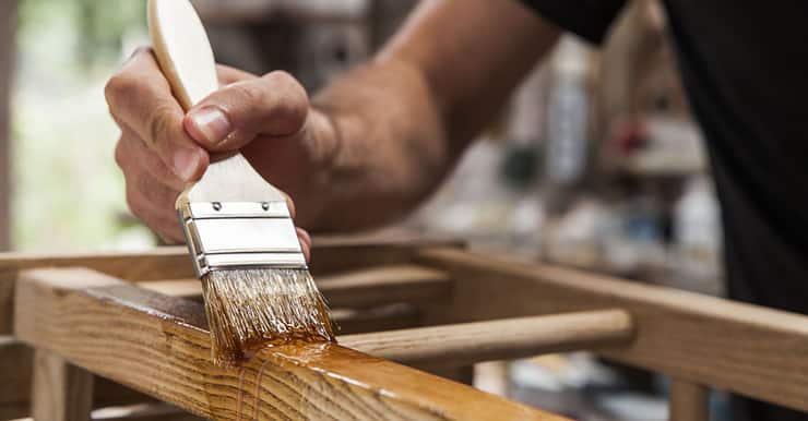 Zoom sur la main d’un homme tenant une brosse et appliquant du vernis sur un mobilier en bois