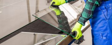 Un homme en combinaison bleu et gants jaunes coupant un panneau de verre